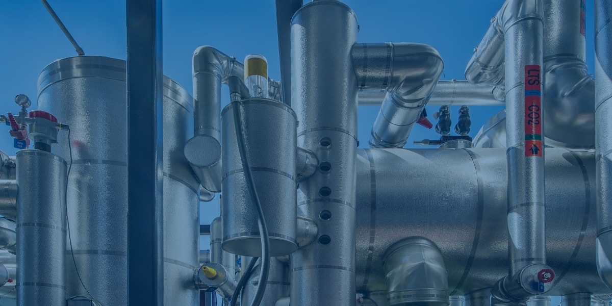 Interconnected insulated metal pipes, valves, and gauges form an industrial piping system set against a clear blue sky.